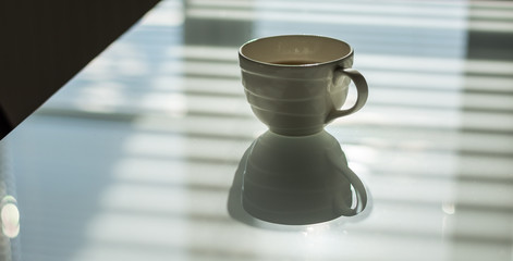 Cup of coffee on the white glass table. Reflections and shadows. Conceptual modern office.