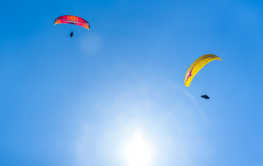 Two paragliders flying against the blue sky with white clouds.