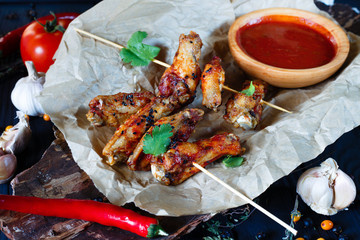 Grilled chicken wings with spicy tomato sauce on craft paper served on bark