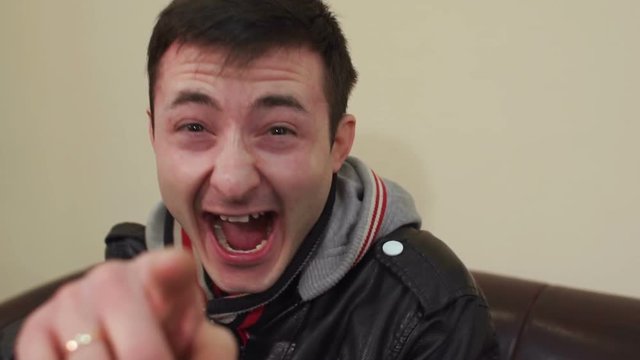 Young man laughs by pointing his finger at the camera, slow motion.