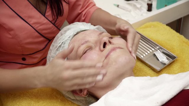 Beautician covering woman's face with gel after the anti aging procedure in salon closeup
