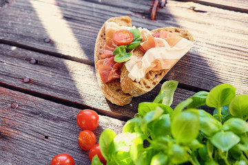 Brown bread with ham, basil and tomatoes on a grey wooden table.