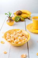 Healthy breakfast with cereal flakes and fruit near vase with flowers on white background. Yellow tone