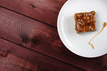 a piece of chocolate brownie and caramel sauce on a white plate. Top view