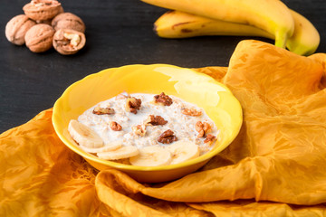 Oatmeal with walnuts and banana in yellow bowl on black background.. Healthy breakfast