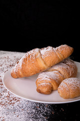 Croissants with powdered sugar and chocolate on white plate on black background. Close up
