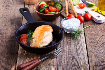 Fried chicken breast on skillet with tomato cucumber salad and yogurt sauce