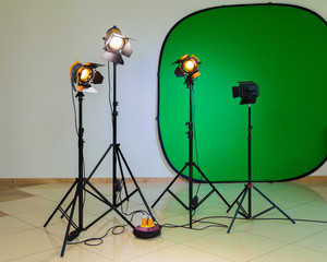 Lighting equipment for filming in the interior. Green background for chromakey. Halogen spotlights with Fresnel lenses. Electrical cables and extension cords.