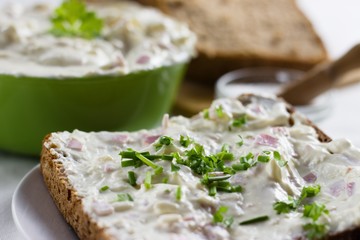 Slice of wholegrain rye bread with delicate light and fresh cottage cheese spread sprinkled with chives and parsley