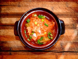 A portion of stewed cabbage with sweet peppers and chopped green onions stands on a brown wooden kitchen board