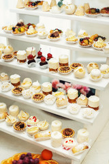 Wedding reception stand with sweets, candies, dessert, cupcakes, muffins, cakes, eclairs decorated with flowers