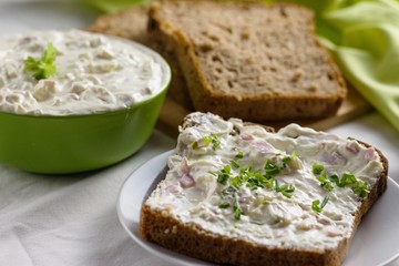 Slice of wholegrain rye bread with delicate light and fresh cottage cheese spread sprinkled with chives and parsley