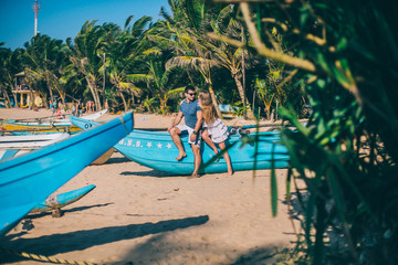 Happy Romantic honeymoon couple on the beach sitting on the sand near old fishing boat and looking...