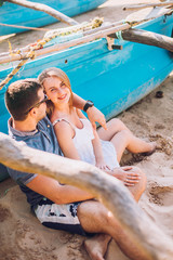 Fototapeta premium Happy Romantic honeymoon couple on the beach sitting on the sand near old fishing boat and looking each other kissing. Husband with his wife near the ocean. Sri lanka. Hikkaduwa.