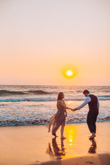 Fototapeta premium Honeymoon couple romantic in love at beach sunset. Newlywed happy young couple holding hands enjoying ocean sunset during travel holidays vacation getaway.