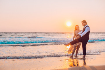 Fototapeta na wymiar Honeymoon couple romantic in love at beach sunset. Newlywed happy young couple holding hands enjoying ocean sunset during travel holidays vacation getaway.