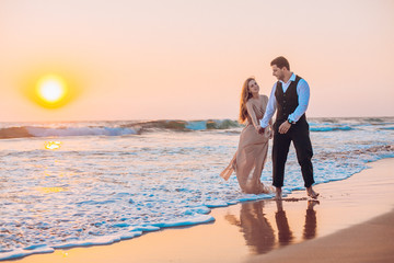 Honeymoon couple romantic in love at beach sunset. Newlywed happy young couple holding hands enjoying ocean sunset during travel holidays vacation getaway.