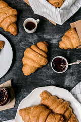 Picture of croissants, pot with jam and coffee cup aside on grey table