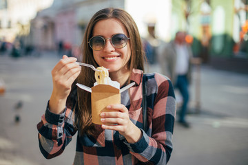  Beautiful smiling young female in sun glasses eating fast food on cities background