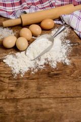 Flour, eggs, salt, towel, rolling pin on wooden table ready for cooking
