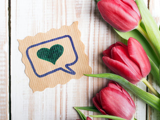 A bouquet of tulips and ornamental card with heart on a wooden background