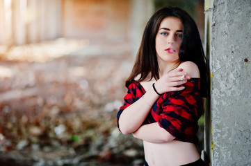 Portrait smoking girl with red lips wearing a red checkered shirt with bare shoulders posed sexy background abadoned place.