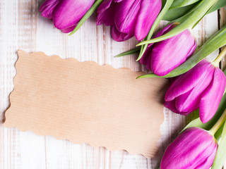 A bouquet of tulips and an empty paper card on wooden background