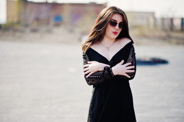 Obraz premium Portrait brunette girl with red lips wearing a black dress posed on the roof. Street fashion model.