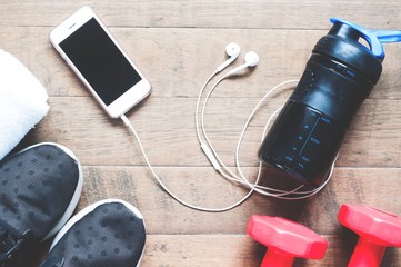 Flat lay of mobile phone with earphones and sport equipments on wood background. Workout and fitness items, top view