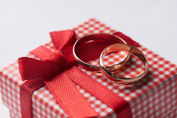 Close-up of two gold Wedding rings and Gift box for wedding with red bow on isolated white background. Love and marriage proposal concept.