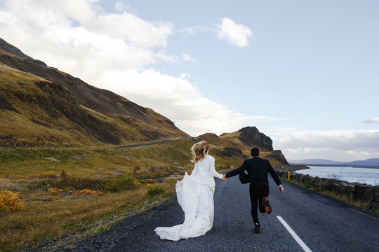 Newlyweds running down highway between river and mountain