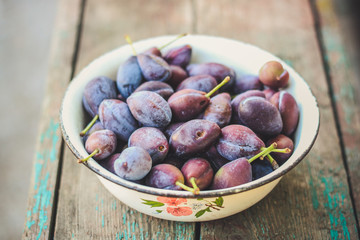 Plums in a bowl on a wooden surface