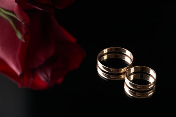 Close-up of two Gold Wedding rings and wedding bouquet of red roses on black background. Gold rings for the bride and groom,  marriage proposal. - Powered by Adobe