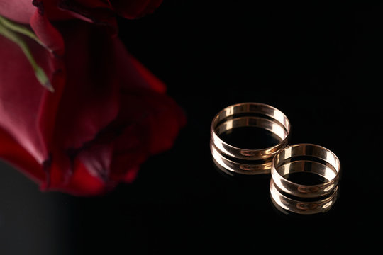 Close-up of two Gold Wedding rings and wedding bouquet of red roses on black background. Gold rings for the bride and groom,  marriage proposal.