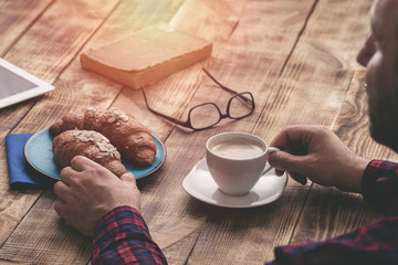 Man has breakfast croissants and drinking coffee at home