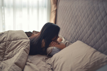 Asian sad depressed woman propped up on pillows on bed