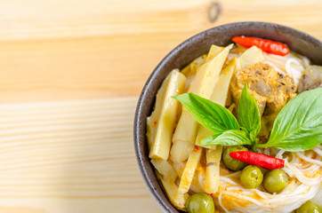 Rice noodles in chicken curry sauce with vegetables on wooden background