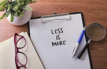 Less Is More word on paper with glass ballpen and green plant.