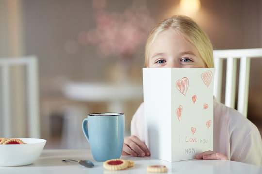 Curious girl peeking out of self-made paper greeting card for mom