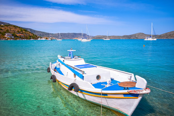 Wooden fishing boat and yachts anchored at the tropical waters of the famous gulf of Elounda, the village of celebrities, near Spinalonga, Crete, Greece.
