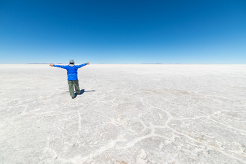 Tourists exploring the world famous Uyuni Salt Flat, among the most important travel destination in the Bolivian Andes. Wide angle view, clear blue sky.