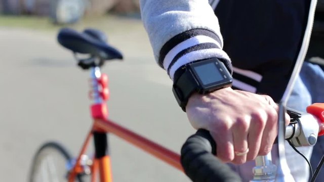 A young man walks down the street with a bicycle, on his hand is a smart watch