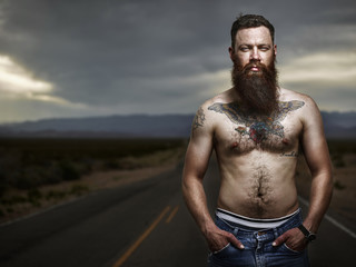 portrait of sexy bearded male hipster standing shirtless in nevada desert wearing only jeans and boxers