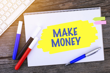 Notebook with MAKE MONEY Handwritten on wooden background and Modern Computer Keyboard. Top View...