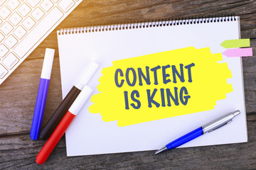Notebook with CONTENT IS KING Handwritten on wooden background and Modern Computer Keyboard. Top View Composition.