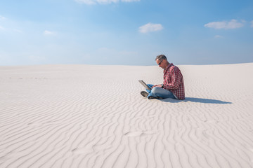 Man is passionate about work, with a laptop sits in desert
