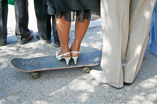 Cropped image of Female Legs in white elegant shoes stand on a black skateboard and male legs next