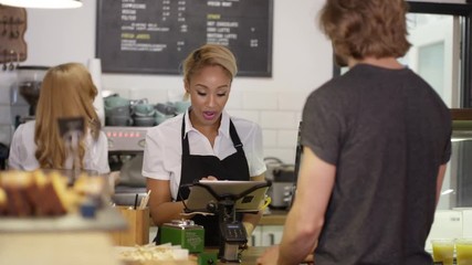  Cheerful worker serving customers & taking payment in city coffee shop - Powered by Adobe