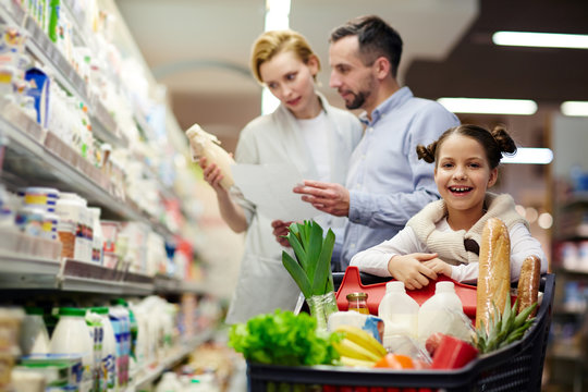 Girl looking at camera in supermarket on background of her parents choosing dairy products