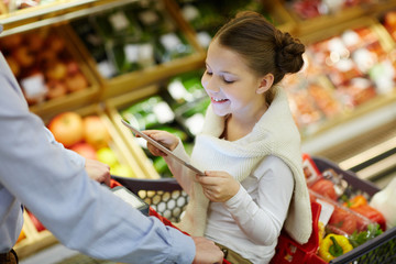 Little girl with touchpad sitting in shopping-cart